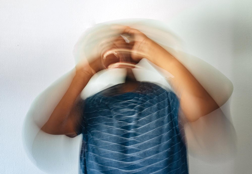 Blurred image of a person holding their head with both hands, suggesting stress, overwhelm, or emotional distress against a plain white background.